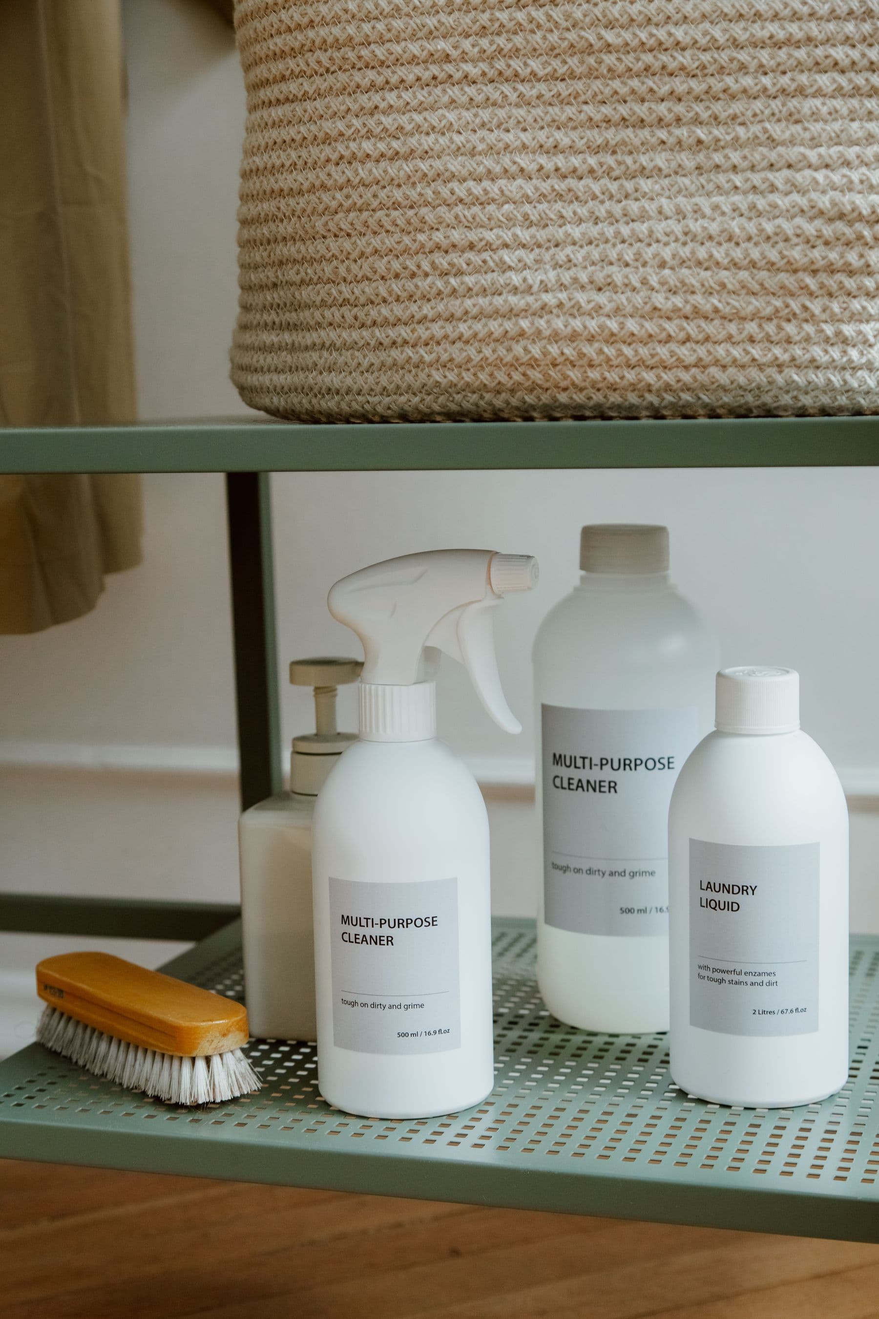 Labelled cleaning products stored in order on a shelf beside a brush.