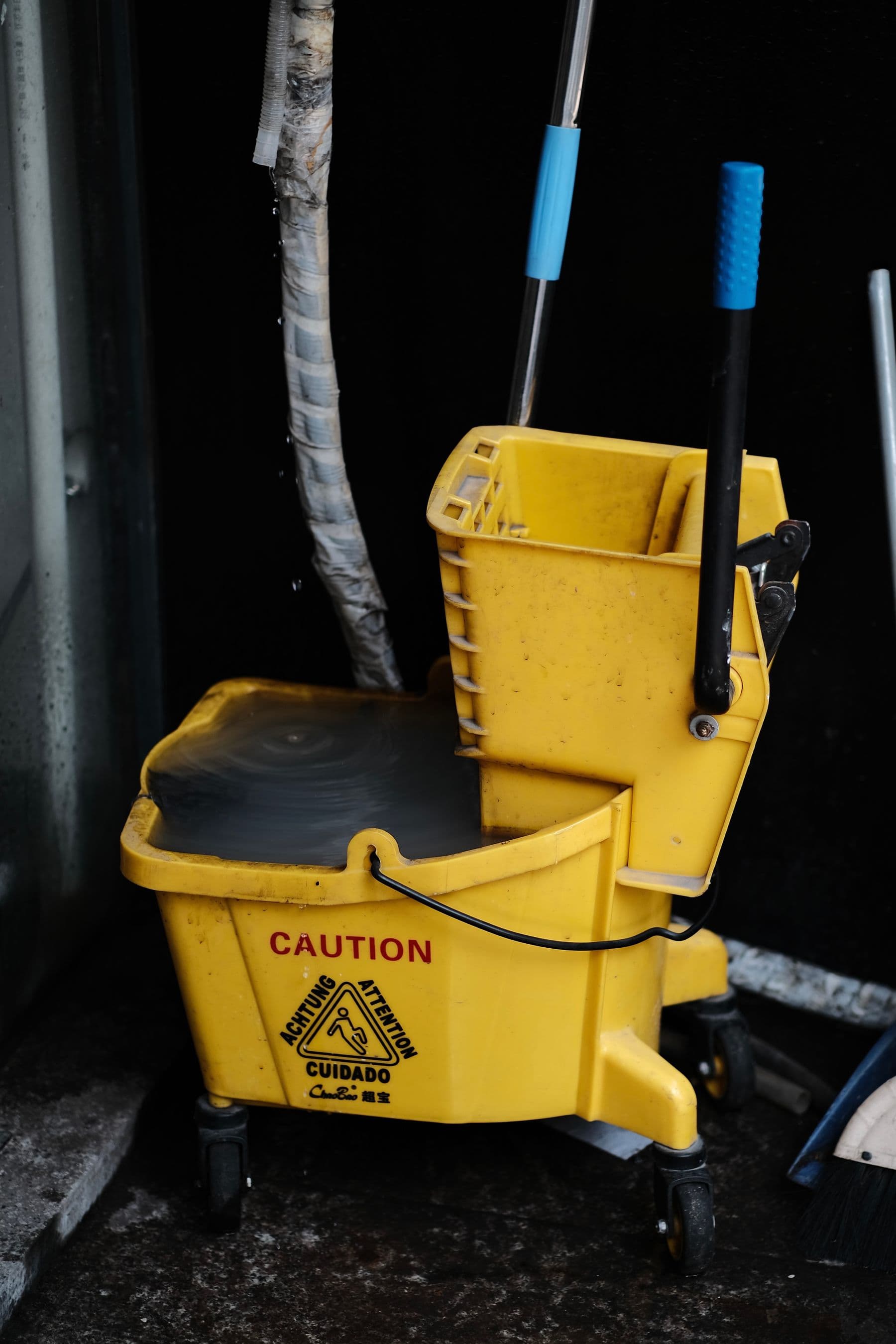 A yellow mop bucket and wringer marked with caution signage, ready for a wet-floor task.